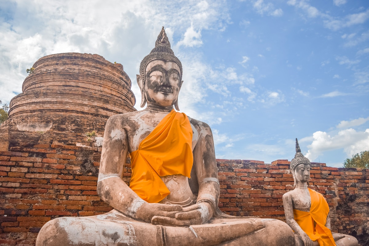 Ancient Buddha statues draped in orange robes among brick ruins at Ayutthaya Historical Park