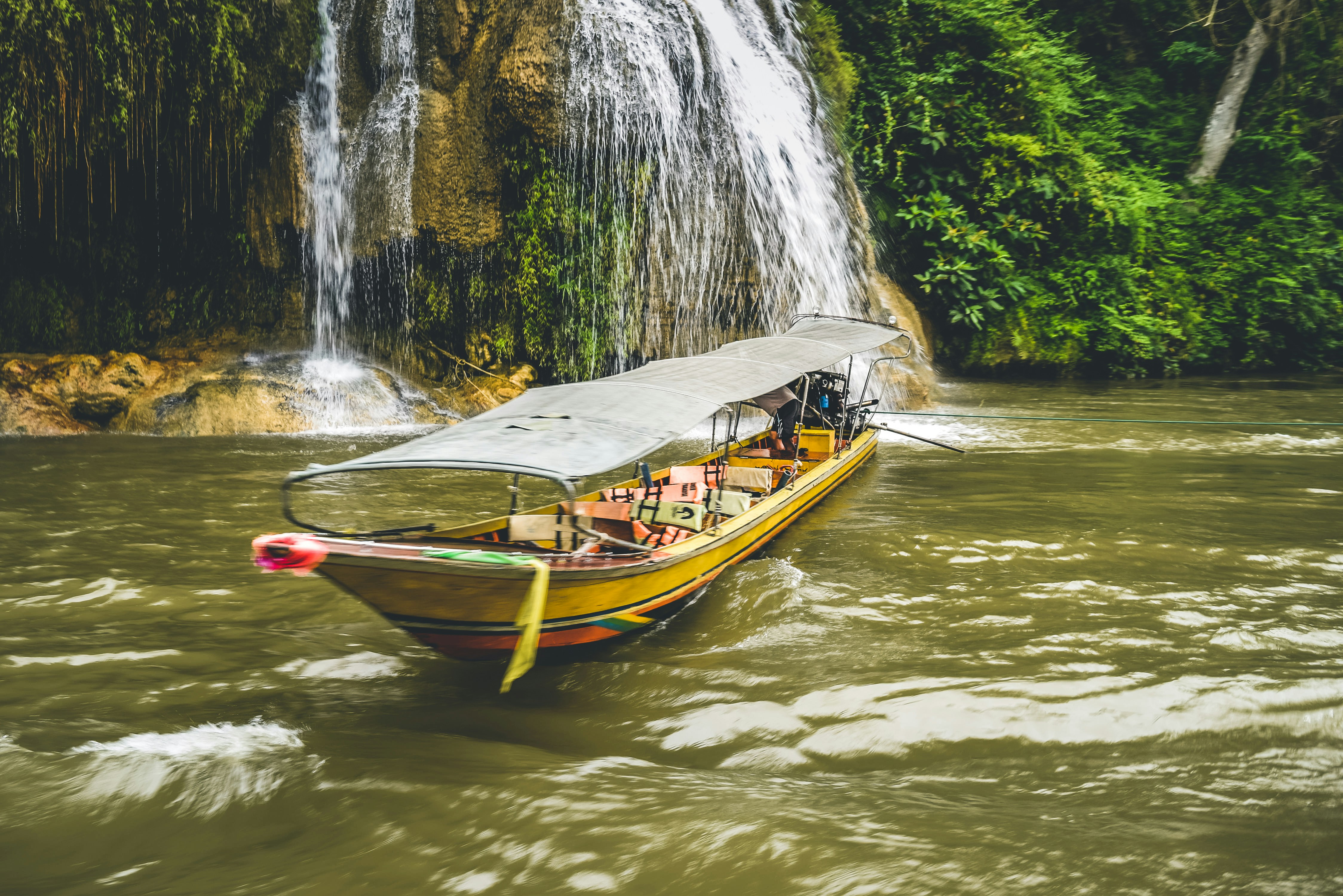 Yellow longtail boat touring past Erawan Falls in lush jungle, Kanchanaburi, Thailand
