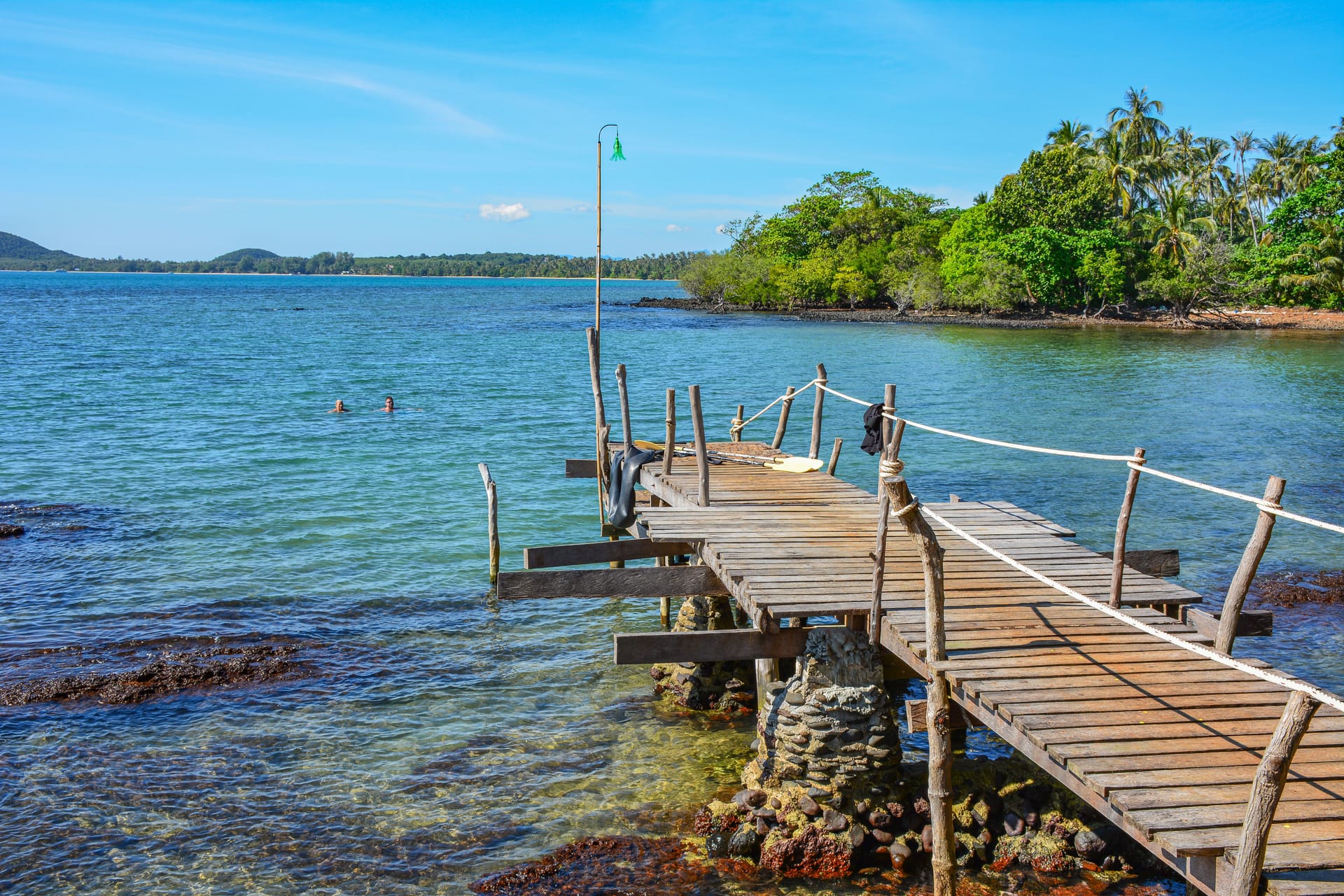 Rustic wooden pier extending into turquoise water with lush tropical jungle, Trat province, Thailand