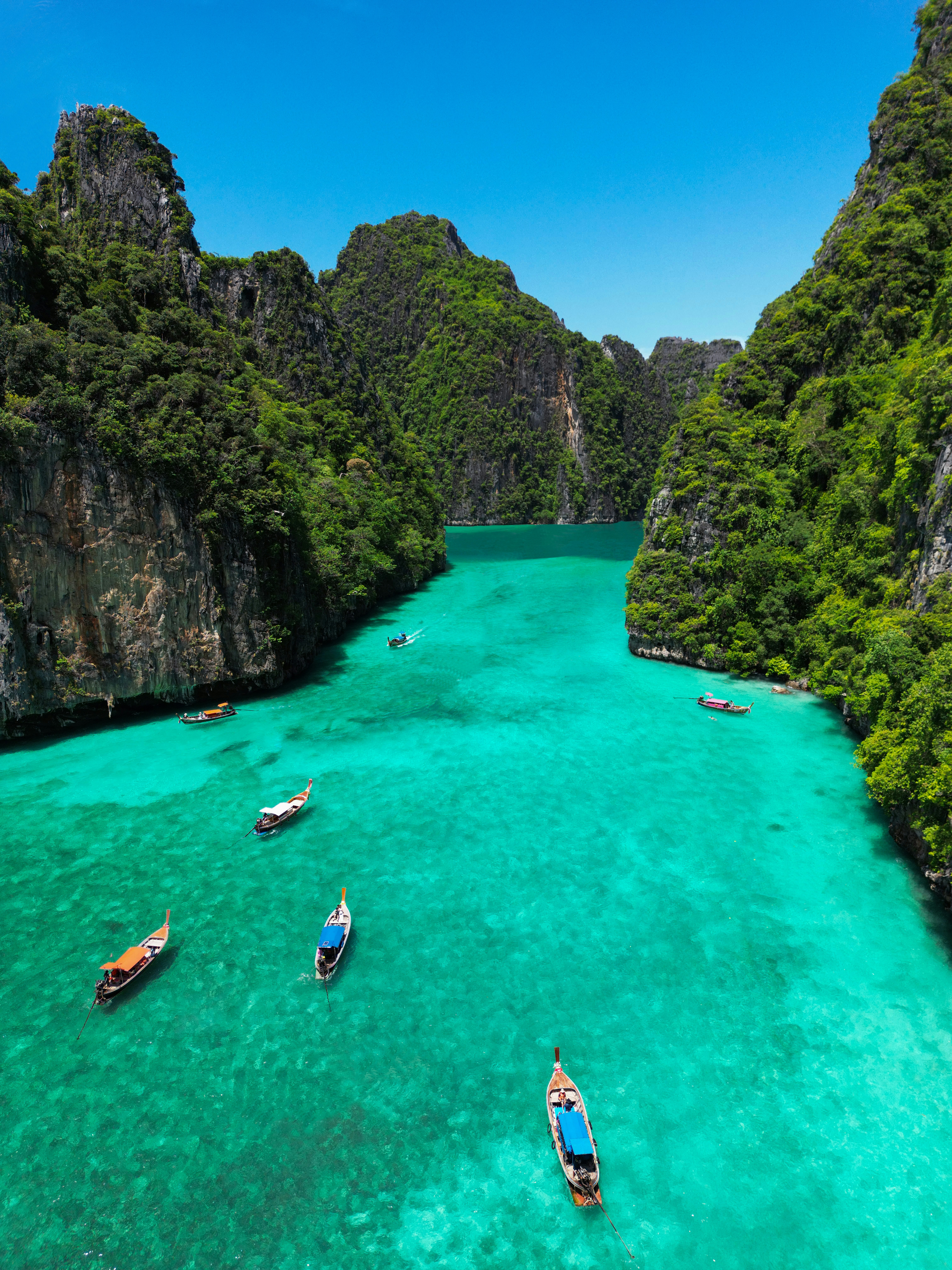 Longtail boats on the turquoise water of Pileh Lagoon surrounded by towering limestone cliffs, Krabi