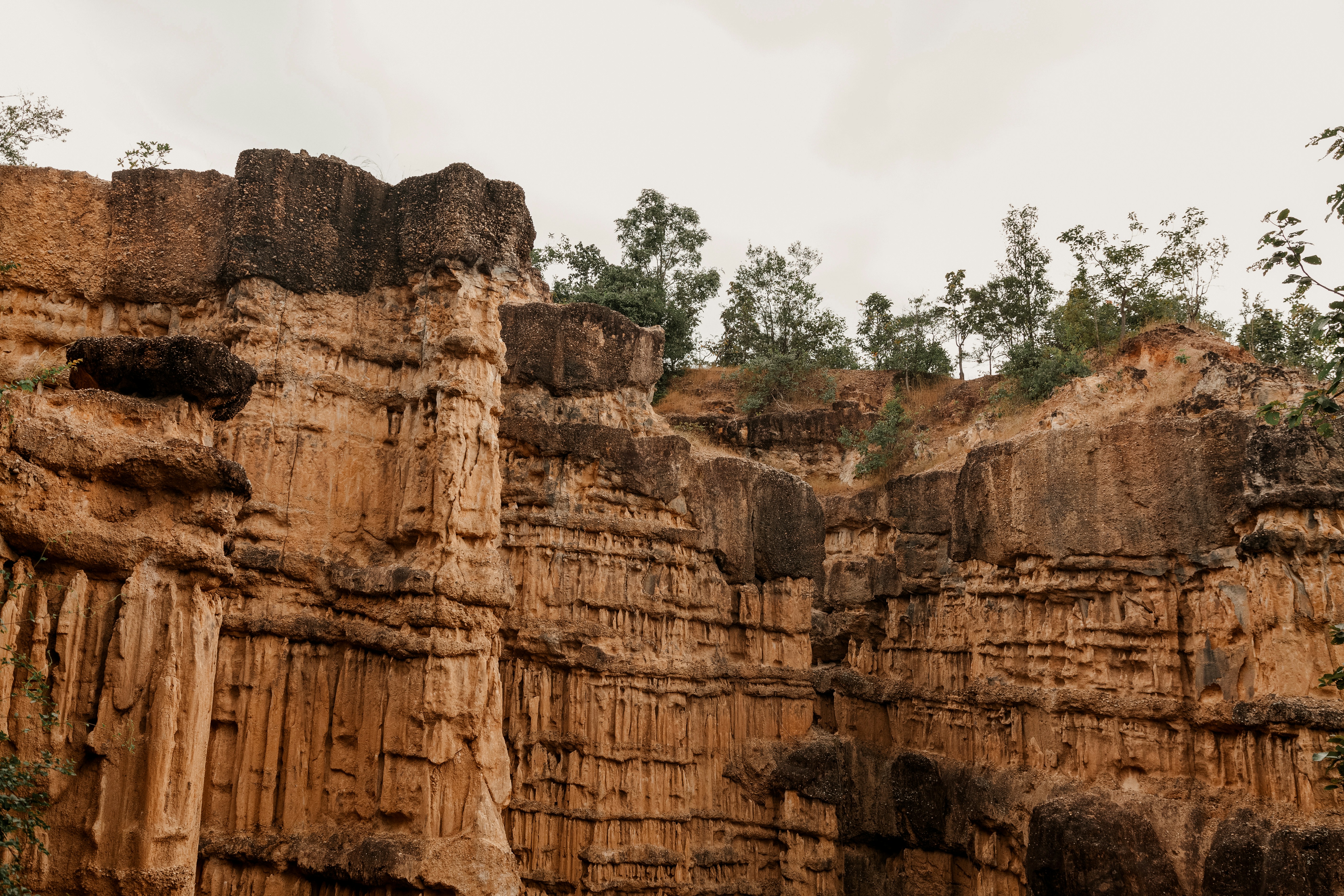 Tall sandstone canyon cliffs with trees under cloudy sky, Pai Canyon, northern Thailand