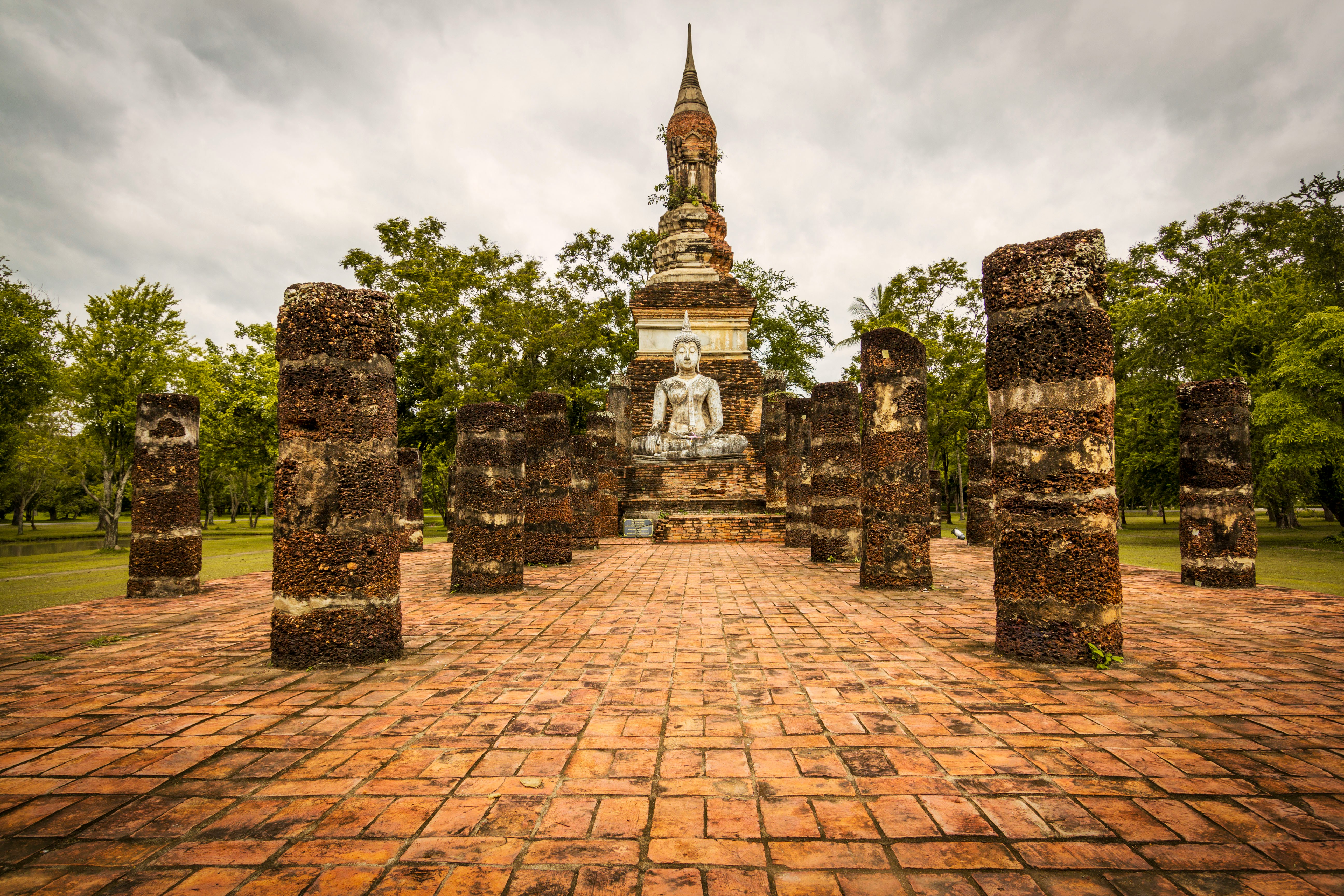 Brick columns leading to a seated Buddha and chedi at Sukhothai Historical Park, Thailand