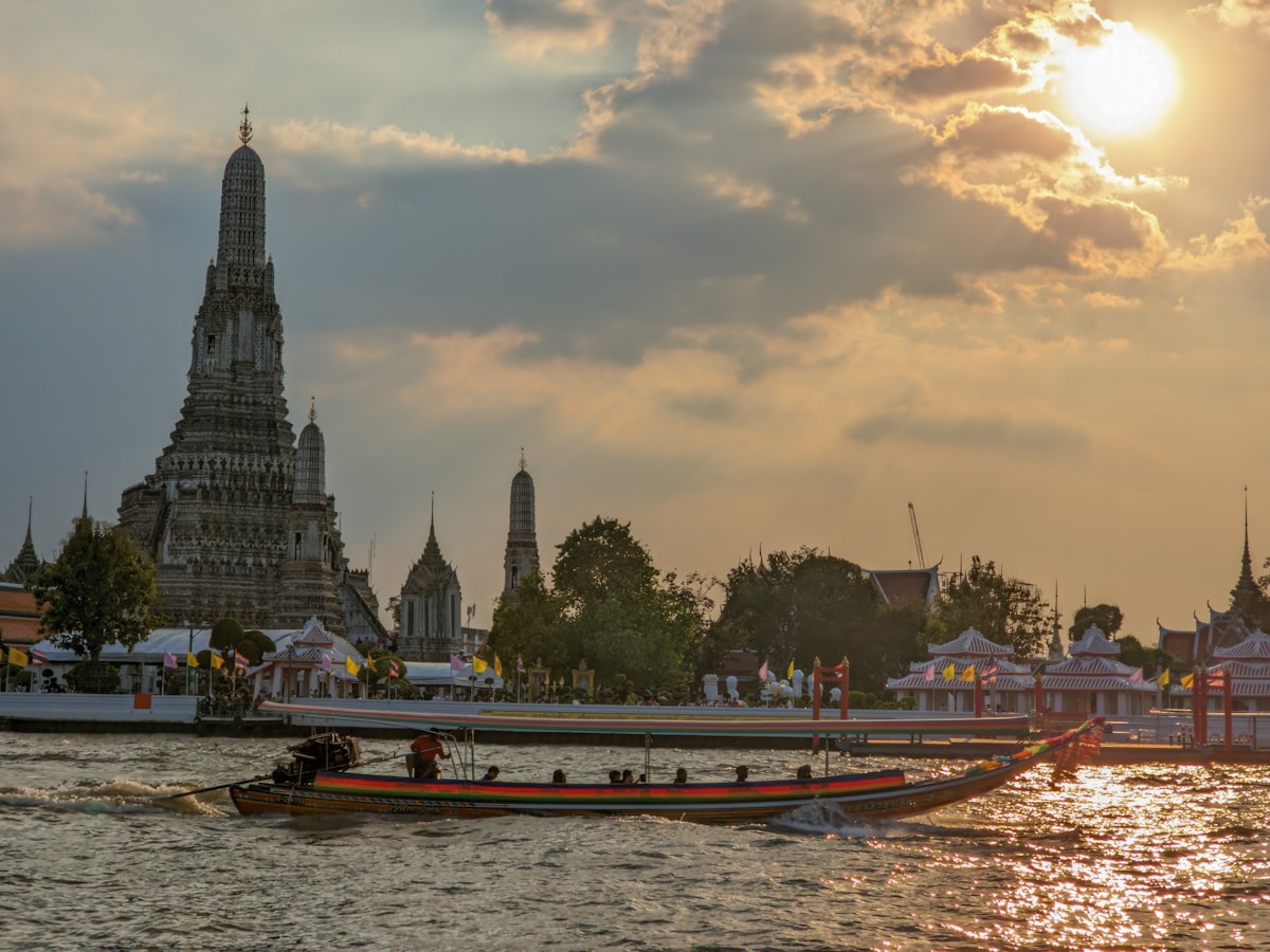 Longtail boats on the Chao Phraya River with Wat Arun illuminated at sunset, Bangkok
