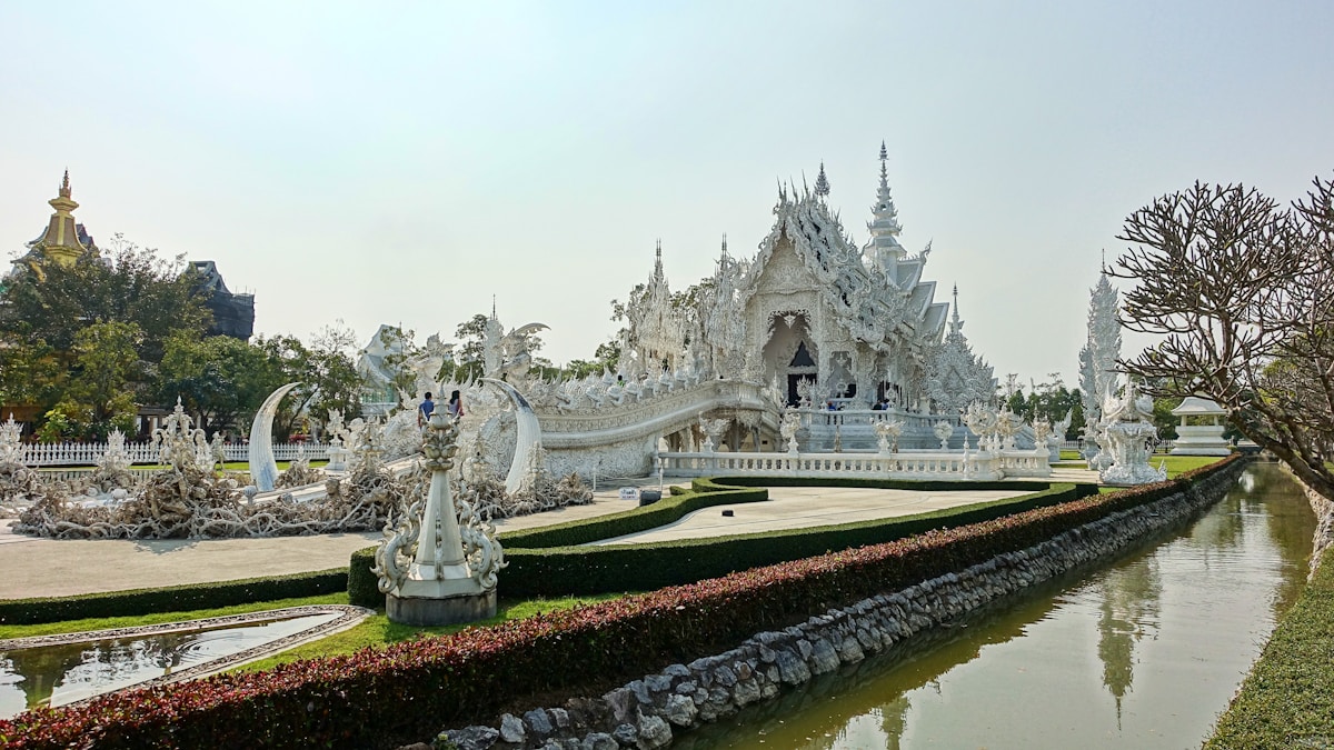 Wat Rong Khun (the White Temple) reflected in a moat surrounded by sculpted white statues, Chiang Rai