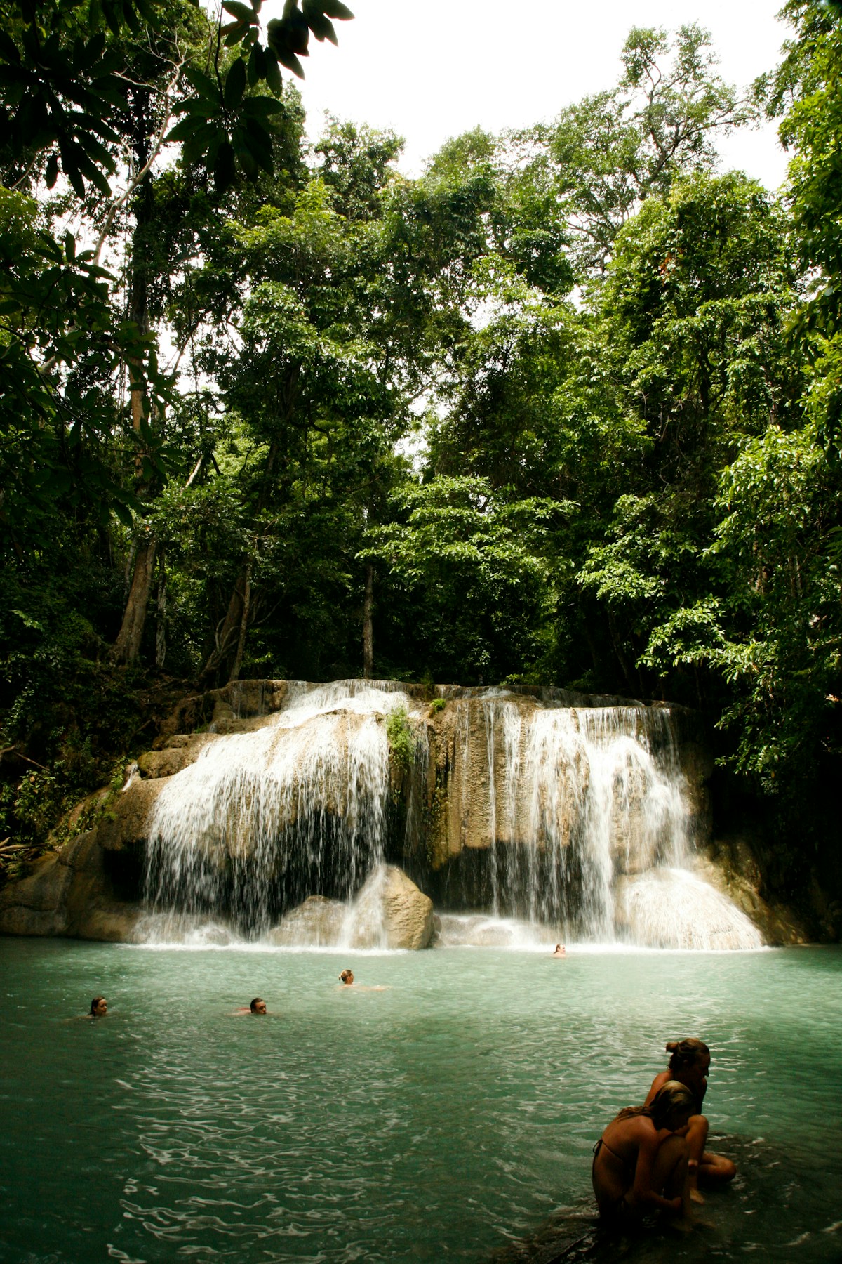 Swimmers in an emerald pool below a multi-tier waterfall in the rainforest at Erawan National Park, Kanchanaburi