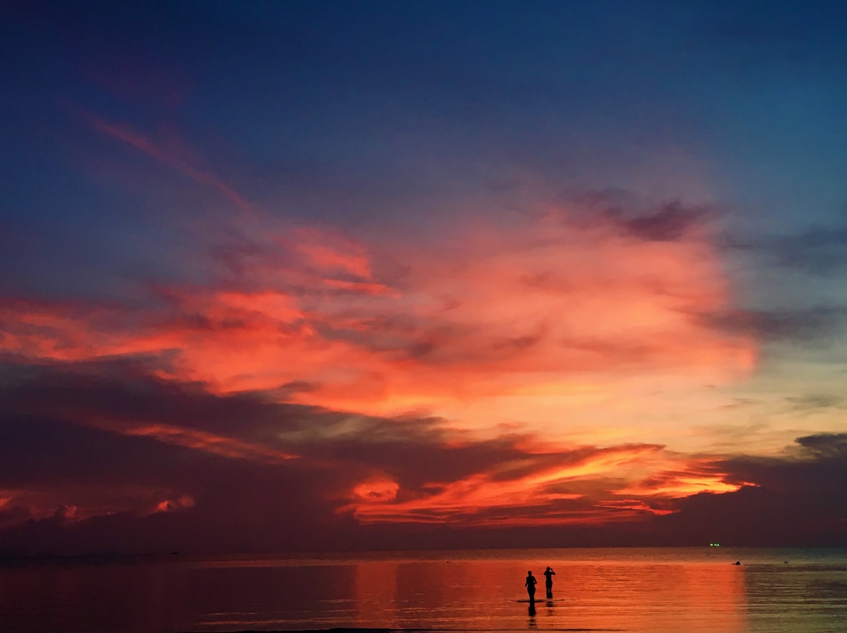 Dramatic sunset over Koh Phangan beach with silhouettes of people at the water's edge