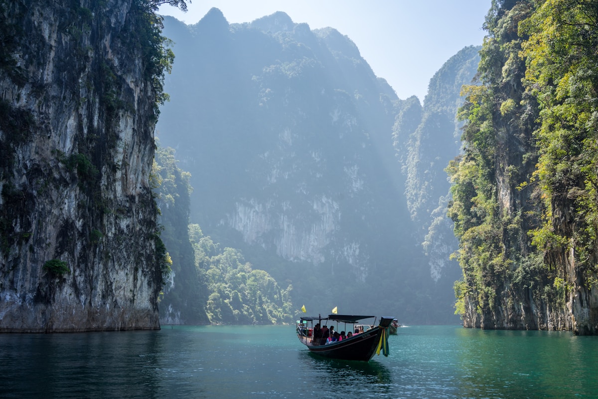 Longtail boat navigating between towering limestone karsts on Cheow Lan Lake, Khao Sok National Park