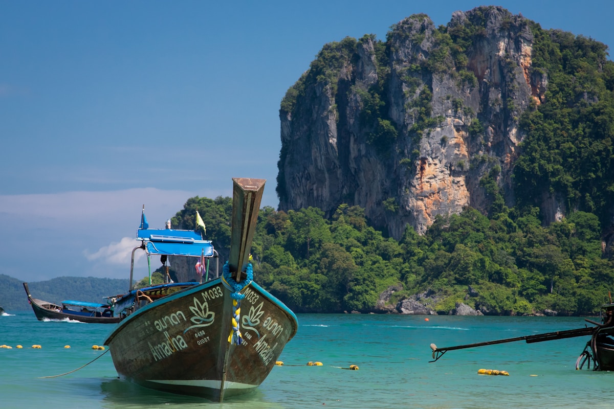 Longtail boat moored in turquoise water with towering limestone cliffs at Railay Beach, Krabi