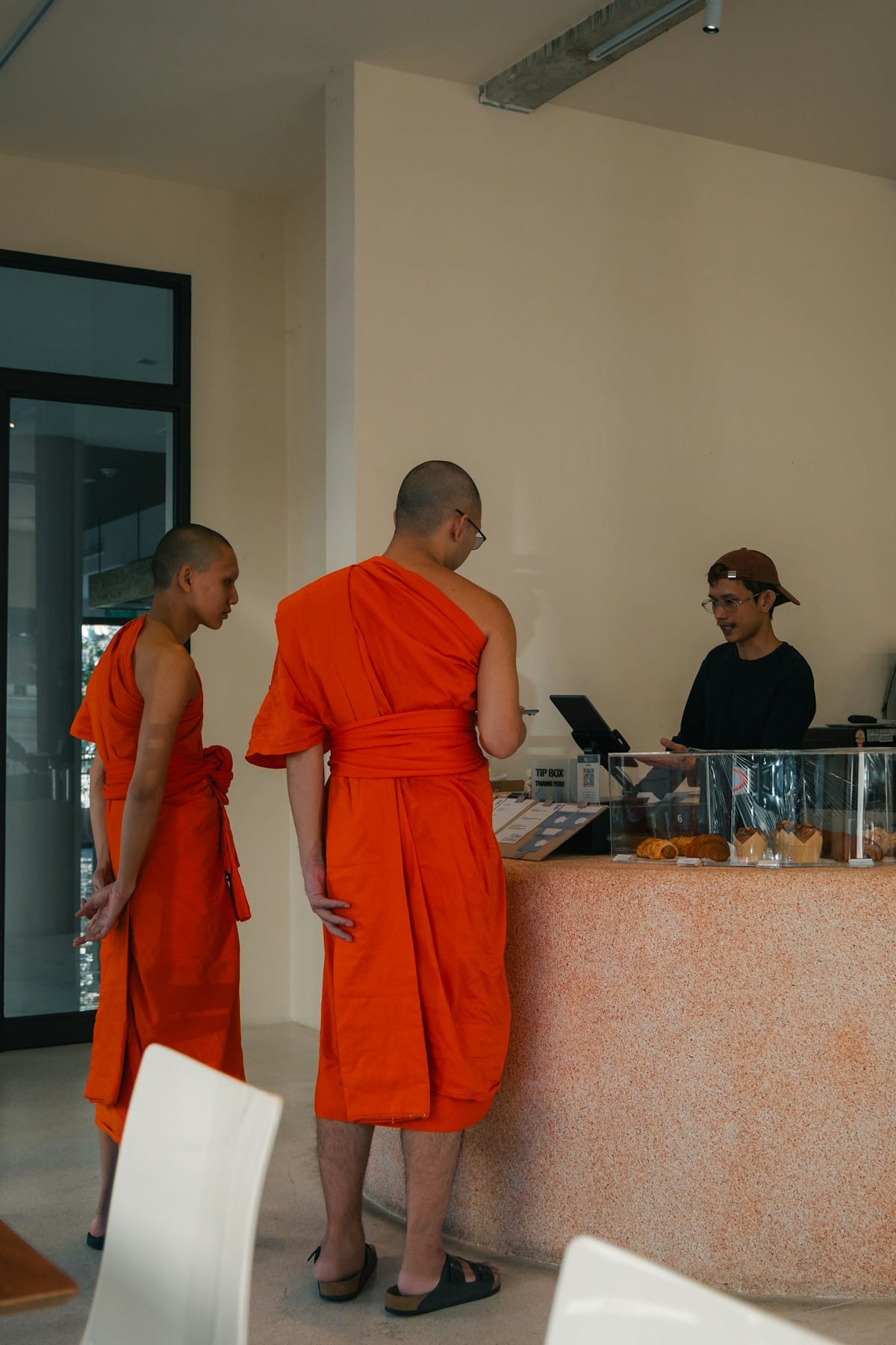 Two monks in orange robes ordering at a Bangkok cafe counter, Thailand