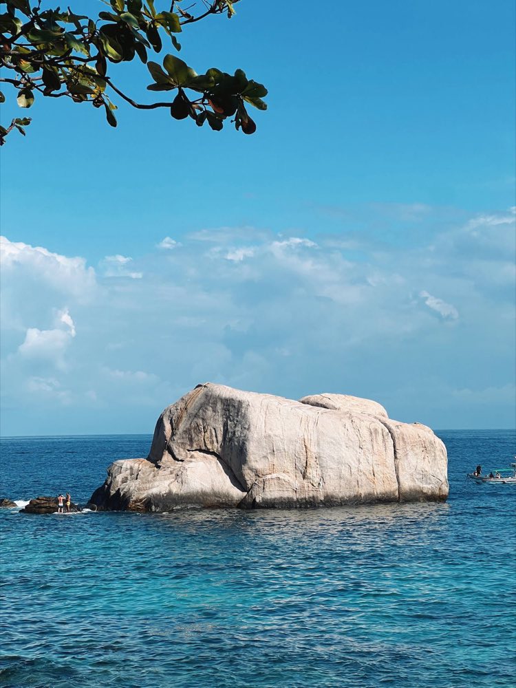 Gros rocher de granit émergeant d'une mer bleue calme sous un ciel dégagé en mer d'Andaman
