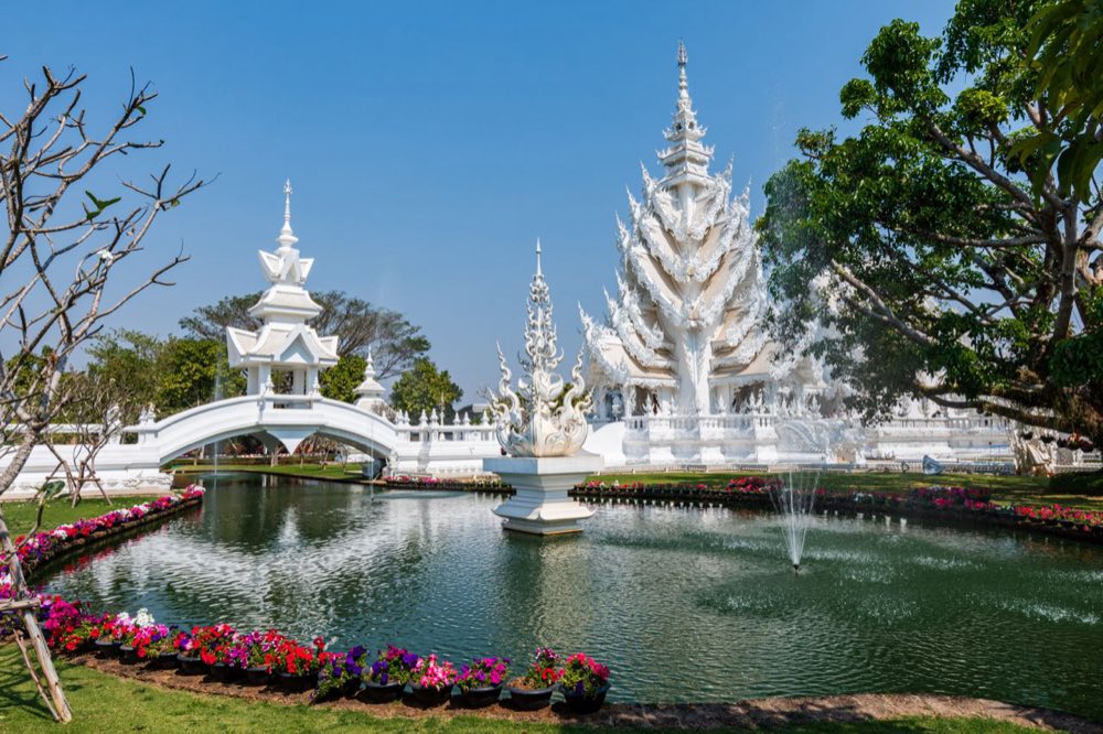 Brücke, Springbrunnenteich und Blumenbeete vor den weißen Türmen des Wat Rong Khun, Chiang Rai