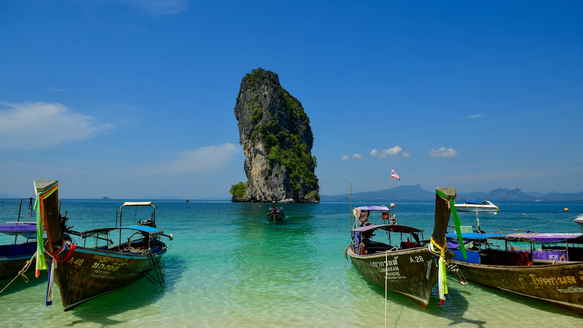 Longtail boats on turquoise water near a limestone rock formation, southern Andaman Sea, Thailand