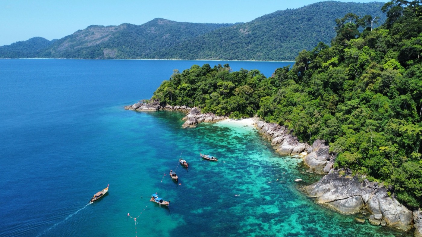 Aerial view of turquoise water and longtail boats along the rocky coastline of Koh Lipe, Satun province, Thailand