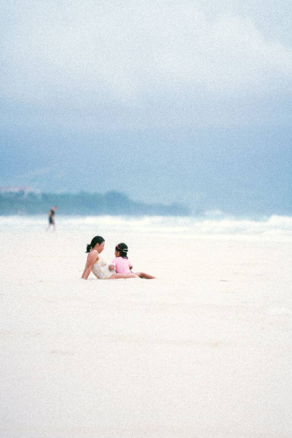 하얀 모래 해변에 앉은 엄마와 아이