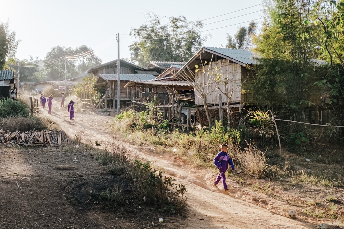 Rural village with wooden houses on stilts and children playing on a dusty lane in northern Thailand