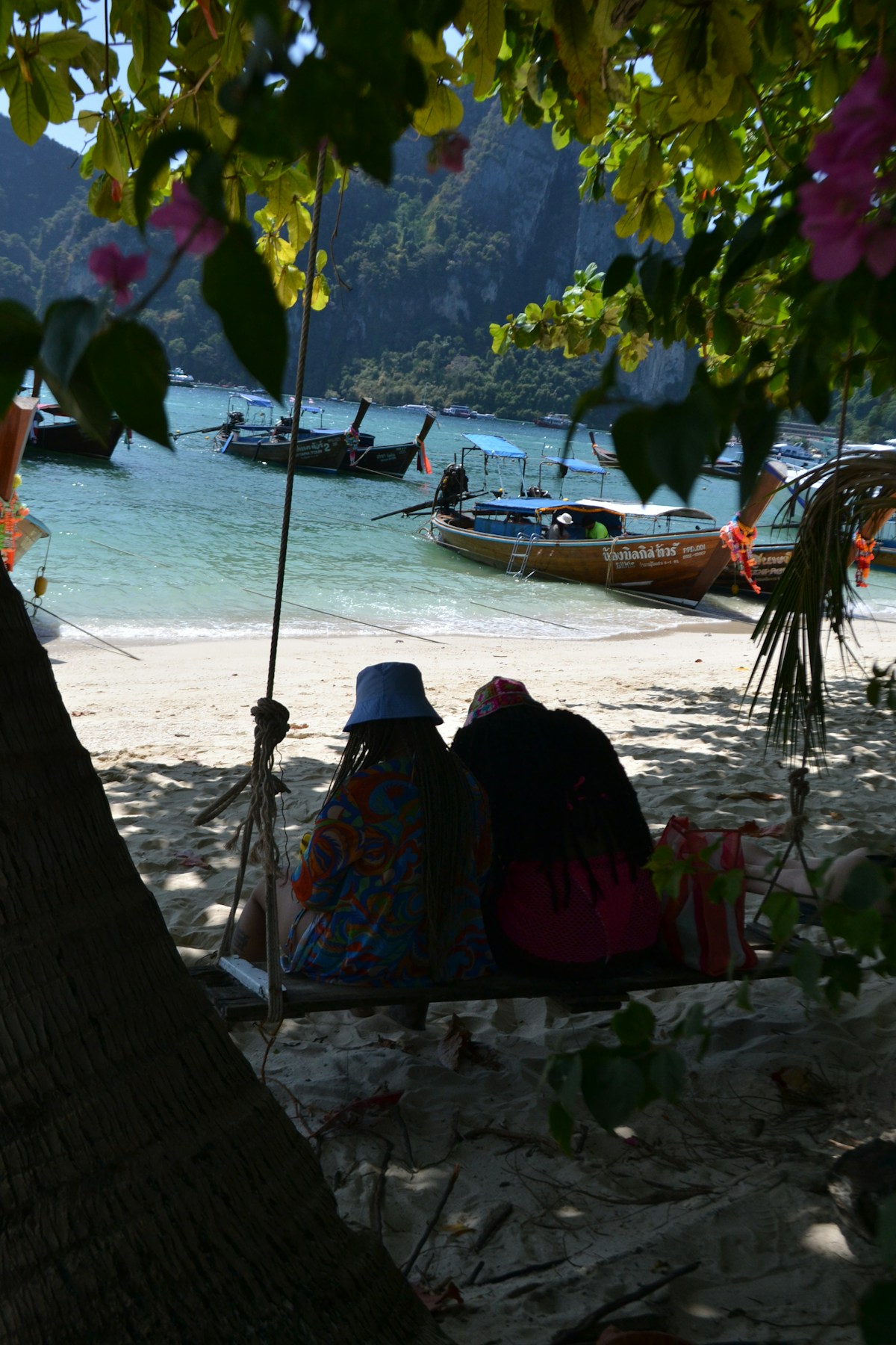 Couple on a beach swing at Phi Phi Islands with longtail boats and limestone karsts, Krabi, Thailand