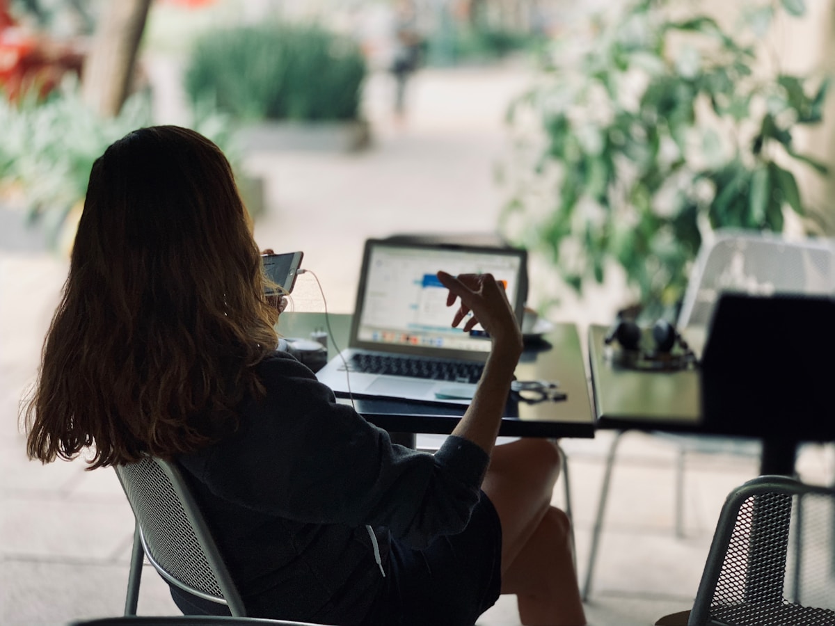 Woman working on laptop at an outdoor cafe with tropical greenery