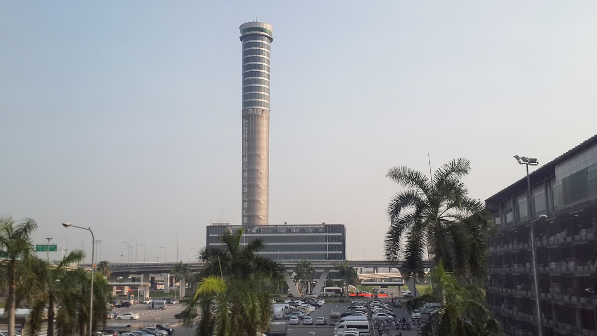 Suvarnabhumi Airport control tower with palm trees and departures road in foreground, Bangkok, Thailand