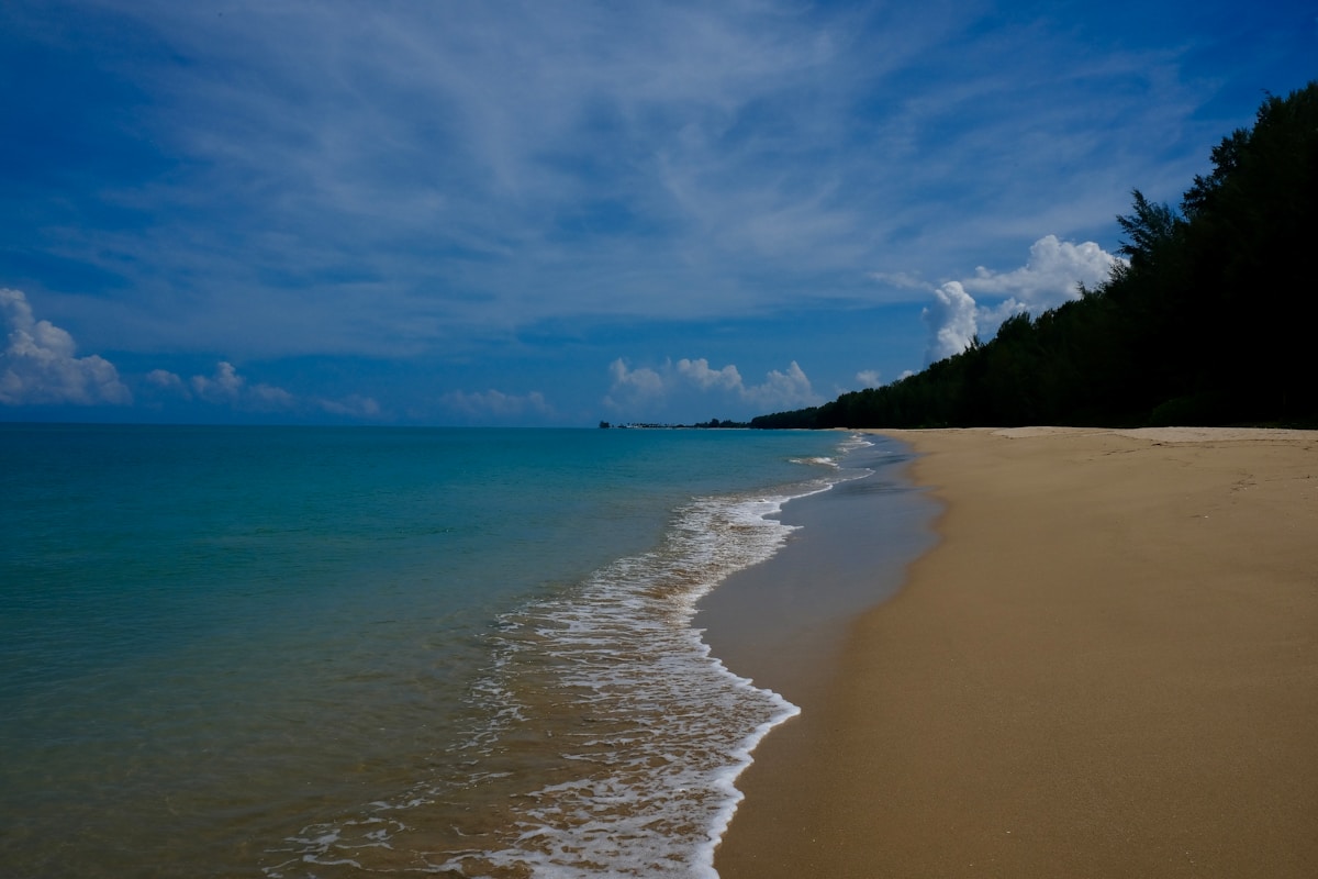 Empty sandy beach with turquoise water and forested coastline at Khao Lak, Thailand