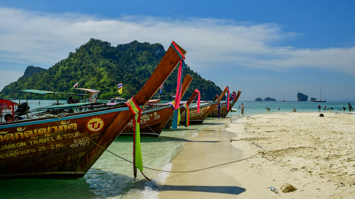 Longtail boats lined up on a sandy beach with limestone karst islands, Krabi, Thailand