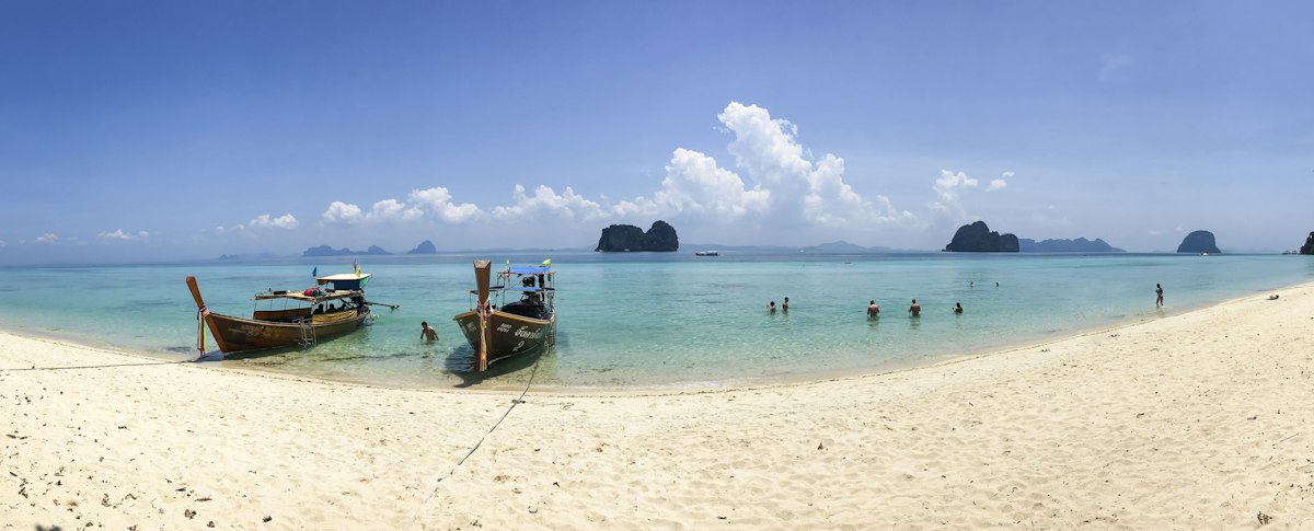 Longtail boats on white sand beach with karst islands in the background, Andaman coast, Thailand