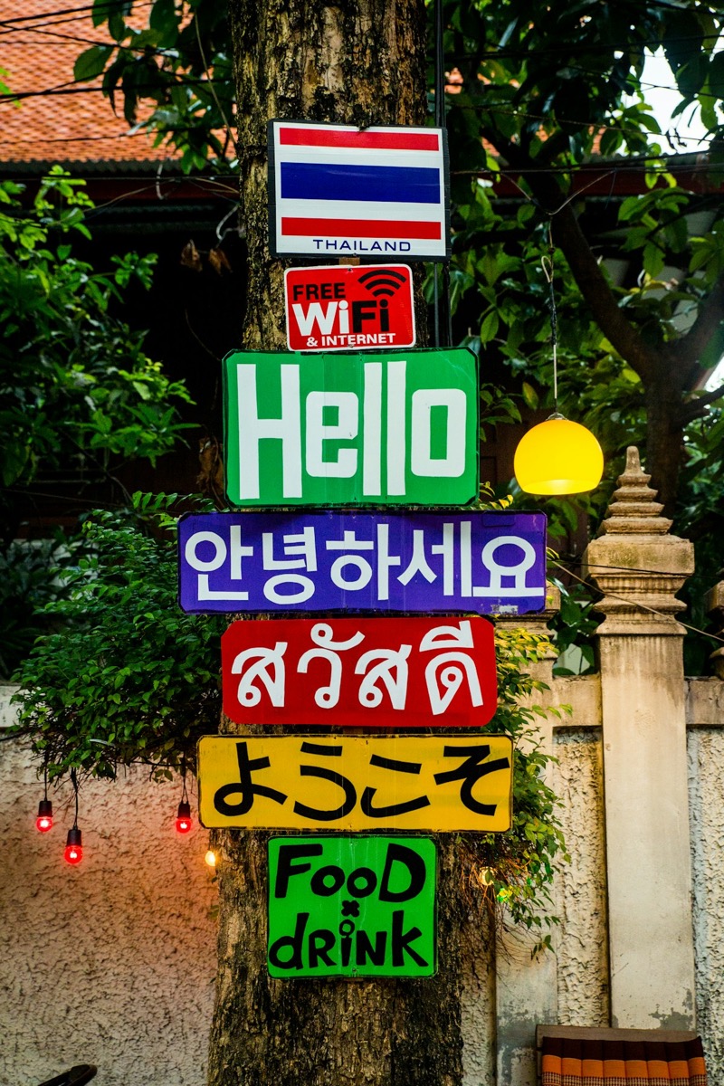 Colourful multilingual street signs including Thai script (สวัสดี) on a Bangkok street