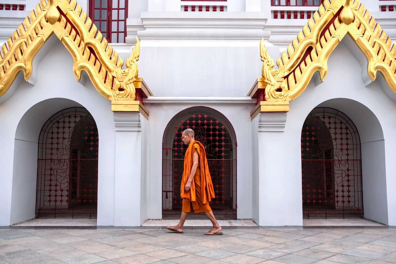 Buddhist monk walking past a white and gold temple building in Bangkok, Thailand