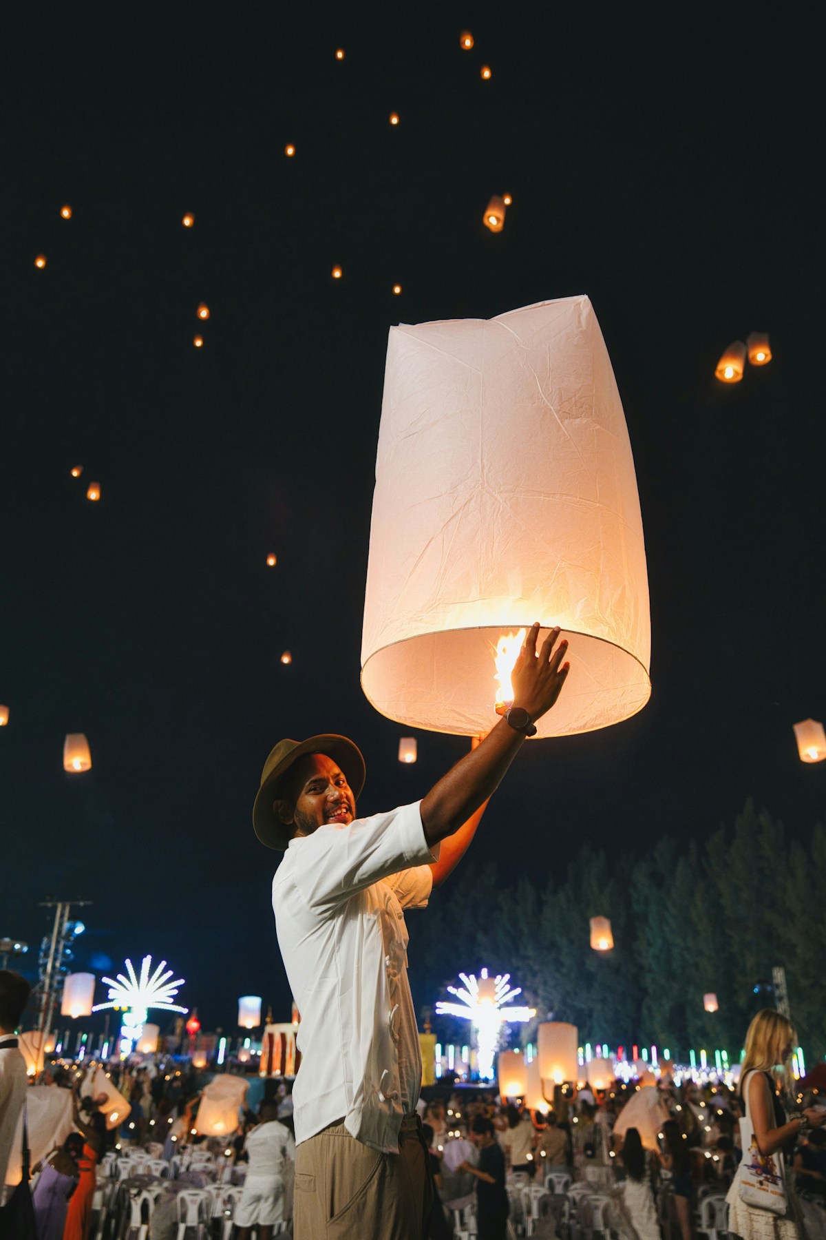 Person releasing a glowing sky lantern into a sky filled with hundreds of lanterns at a Thai festival