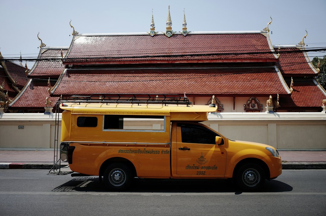 Yellow songthaew parked in front of a traditional Thai temple, Chiang Mai, Thailand