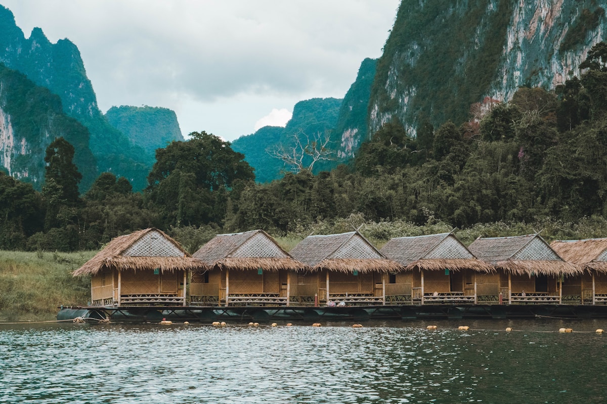 Thatched floating bungalows on calm emerald lake surrounded by limestone karsts, Khao Sok, Thailand
