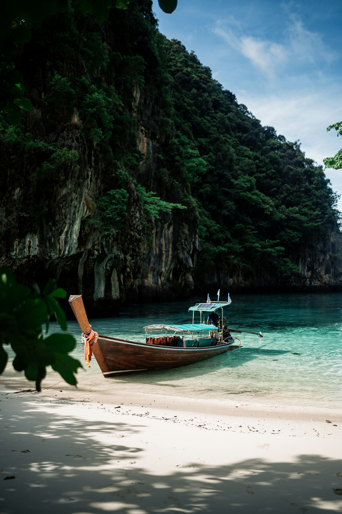 Longtail boat on white sand beach beside towering limestone karst cliffs, Trang province, Thailand